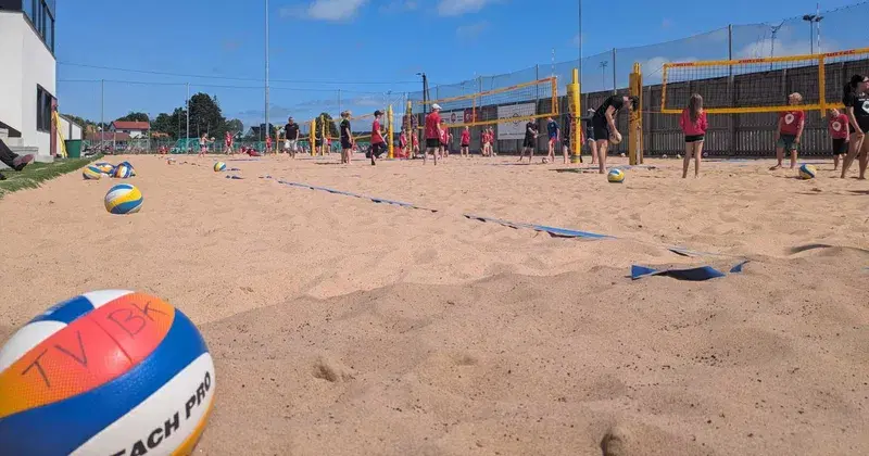 Bilde av sandvolleyanlegget, med en volleyball i forgrunnen og barn i aktivtet i bakgrunnen.